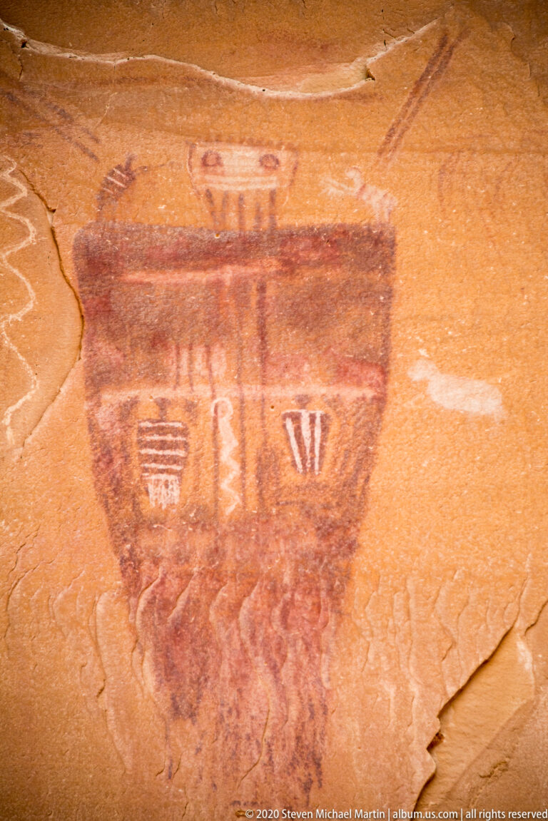 A tapered painted figure contains two pale symbols between dark bands, with an oval mark above.