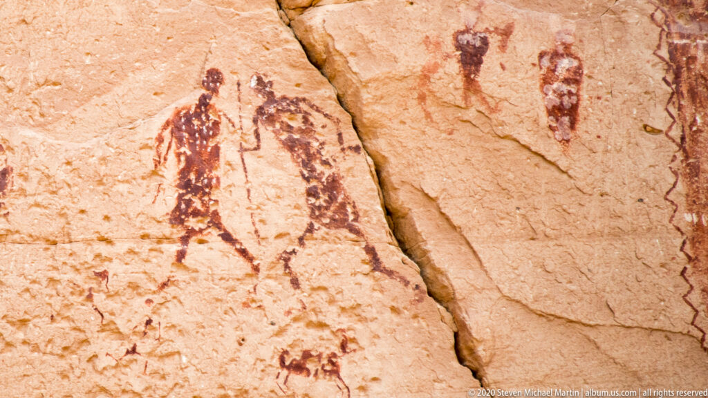Small painted figures and animal-like forms are scattered across a pale, cracked sandstone face.