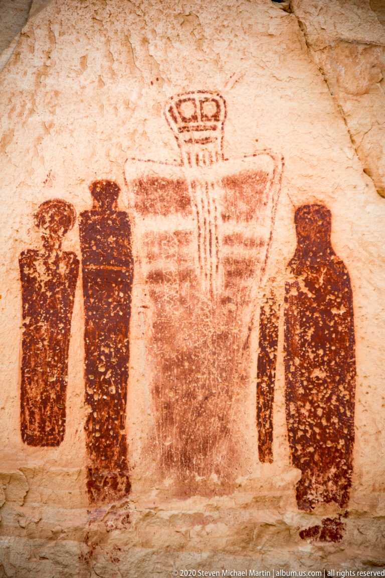 A broad banded figure with a looped top stands between several dark elongated silhouettes.