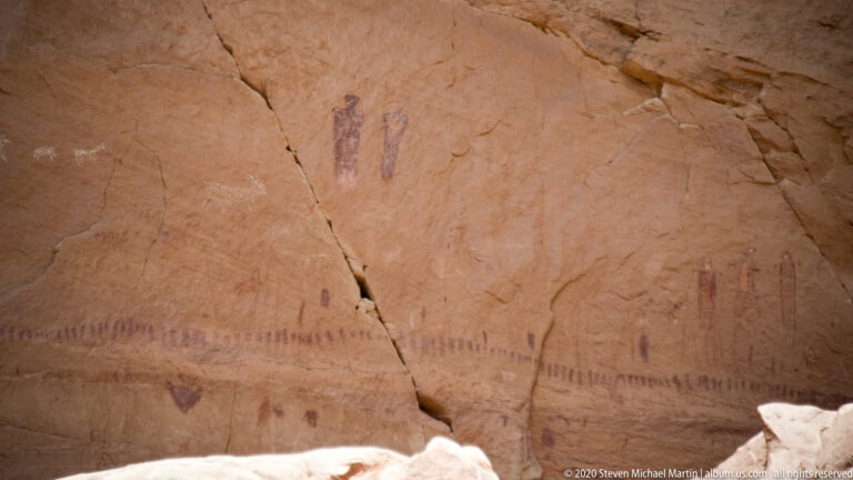 Faded reddish marks form a low band across pale sandstone, divided by a deep vertical crack.