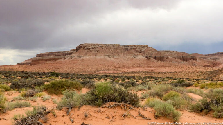 A hiker in blue walks along a grassy trail between tall sandstone cliffs toward a sunlit opening.