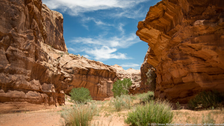 A broad rocky basin with broken ledges and sparse scrub stretches below a distant cliff rim.