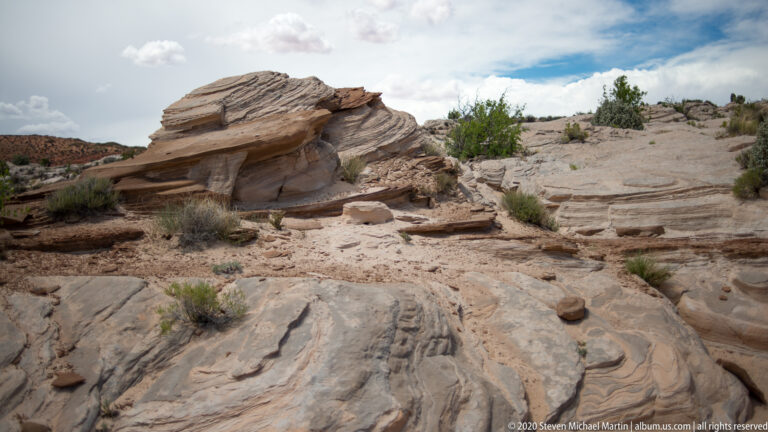 A pale rounded sandstone outcrop rises above stepped shelves and sparse shrubs on an open plateau.