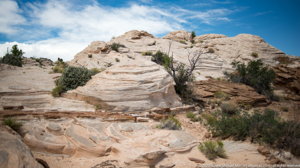 Orange dunes with scattered grass tufts extend toward distant mountains beneath a partly cloudy sky.
