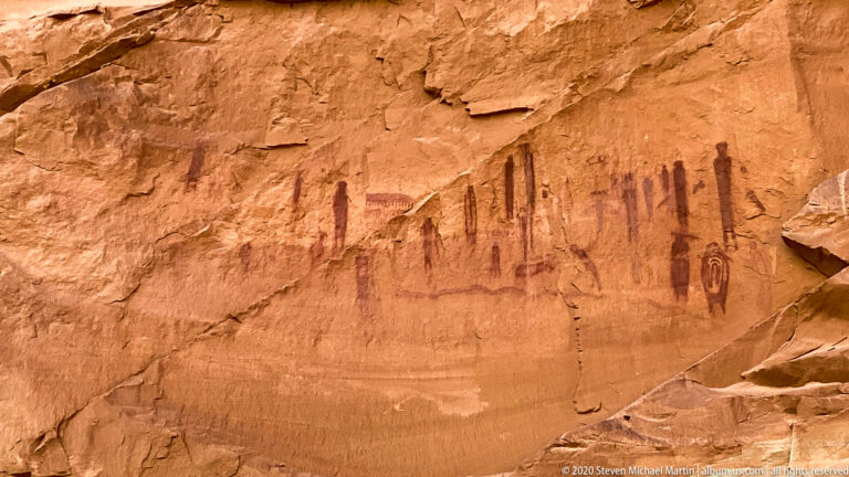 Dark painted human-like figures and circular symbols form a pictograph panel on an orange sandstone wall.