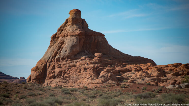 A tall sandstone tower rises above fractured ledges, with a small rounded boulder perched on a nearby shelf.