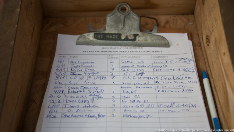 An open visitor register with handwritten entries rests beneath a metal “The Maze” label on a wooden shelf.