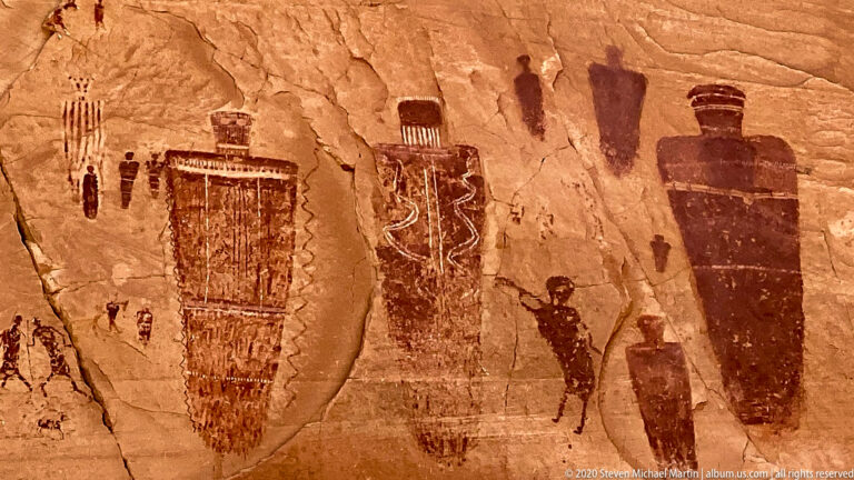 Large dark figures and patterned shapes fill the sandstone, surrounded by smaller painted forms.