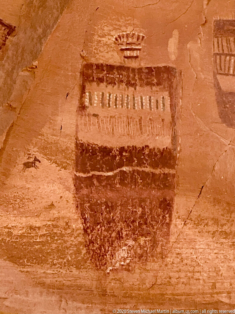 A rectangular dark figure has a band of repeated vertical marks and a small motif above it.
