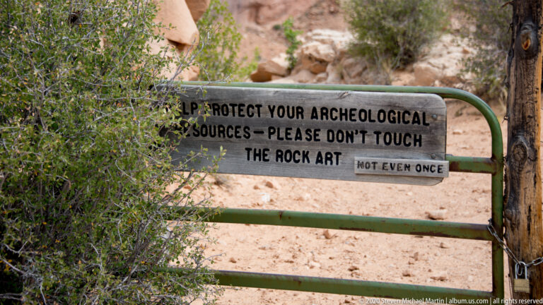 A metal sign on a green gate warns visitors not to touch the rock art.