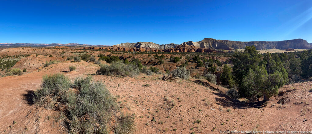 Red and pale sandstone ridges line the horizon above an open basin dotted with junipers and shrubs.