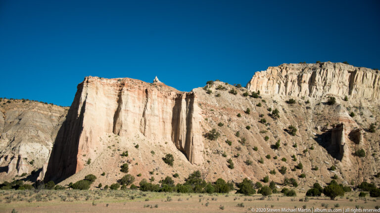 Cream cliffs with deep vertical grooves rise above orange foothills and scattered trees.