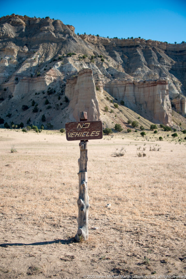 A weathered wooden sign marked “VEHICLES” points across a sandy clearing below pale cliffs.