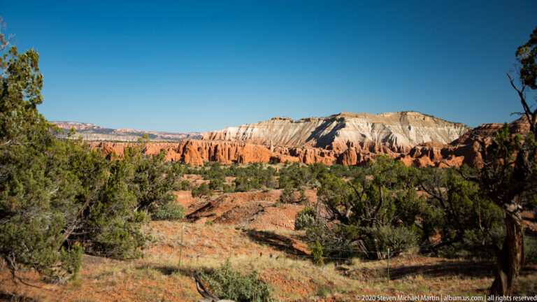 Junipers frame orange ridges and pale cliffs across a layered basin landscape.
