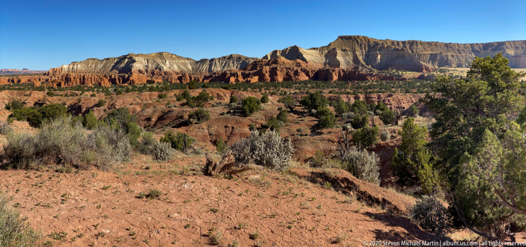 Cream, orange, and red cliffs rise above junipers and sagebrush across the basin.