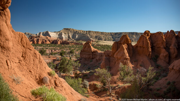 Red sandstone walls frame pointed formations and pale cliffs across an open basin.