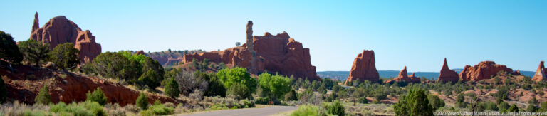 A paved road curves between red sandstone spires and junipers beneath a clear sky.