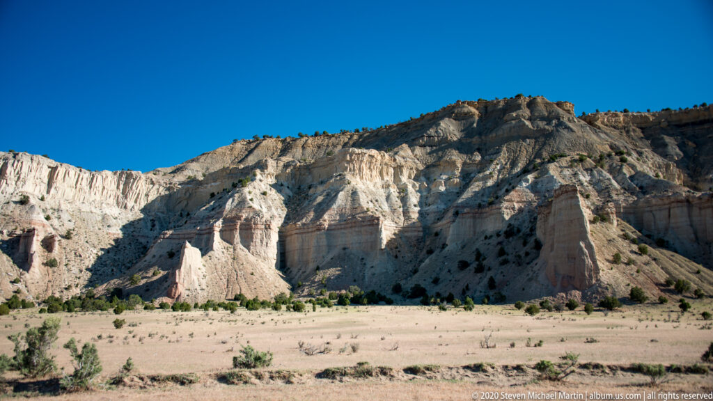 Pale, vertically eroded cliffs form an amphitheater above a flat sandy basin.