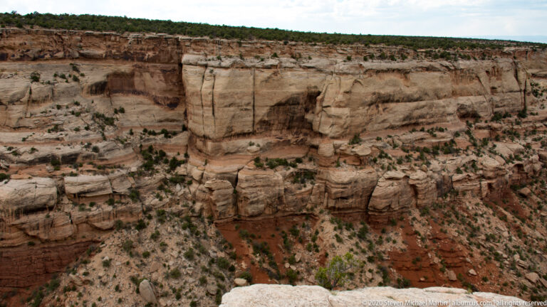 A pale sandstone cliff shows horizontal ledges, vertical cracks, and a dark recess.
