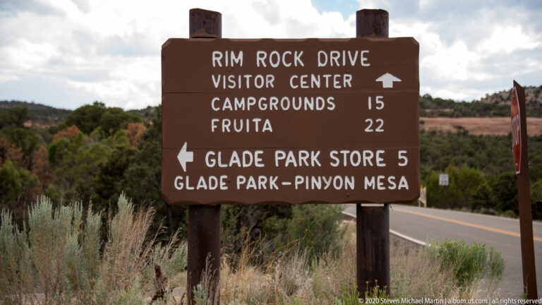 A brown roadside sign lists Rim Rock Drive, Visitor Center, campgrounds, Fruita, and Glade Park.