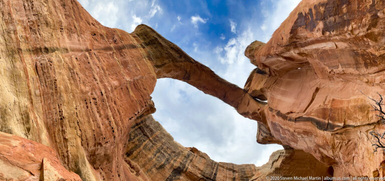 A sandstone arch bridges tall, streaked walls above a narrow opening to the sky.