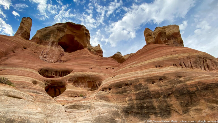 Several dark alcoves and narrow holes punctuate a curved, banded sandstone face.