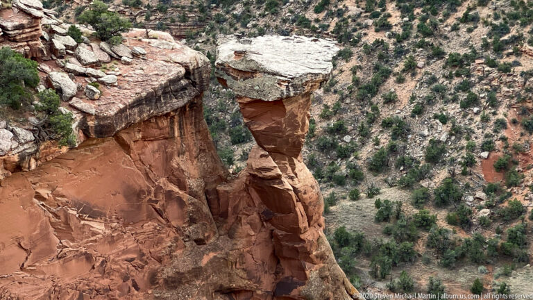 Two thin sandstone pedestals support broad pale capstones above a canyon slope.