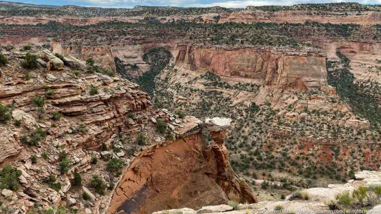 A capstone-topped sandstone pedestal stands above a broad canyon with layered walls.