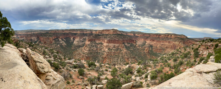 Pale boulders frame a deep canyon with red cliffs and a green, rocky valley below.