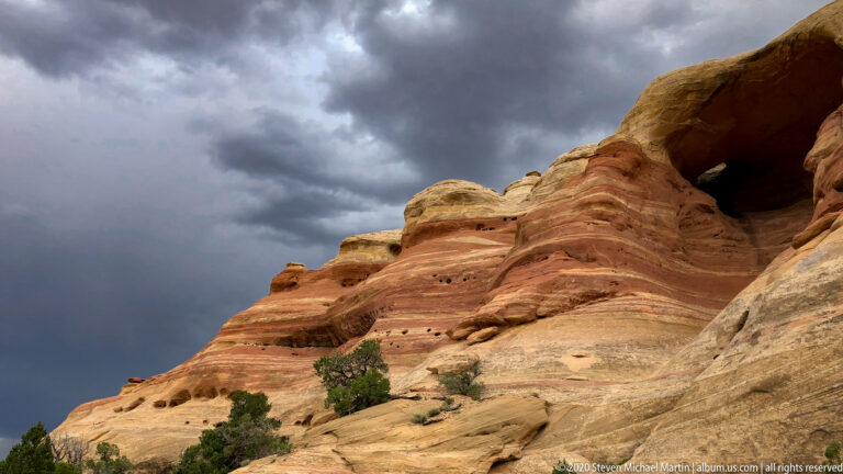 A dark alcove opens beneath a projecting sandstone ledge against a stormy sky.