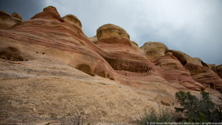 Rounded sandstone domes with rose and cream bands rise beneath a cloudy sky.