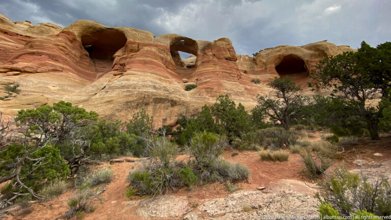 Several dark openings punctuate a long sandstone ridge above juniper and sagebrush.