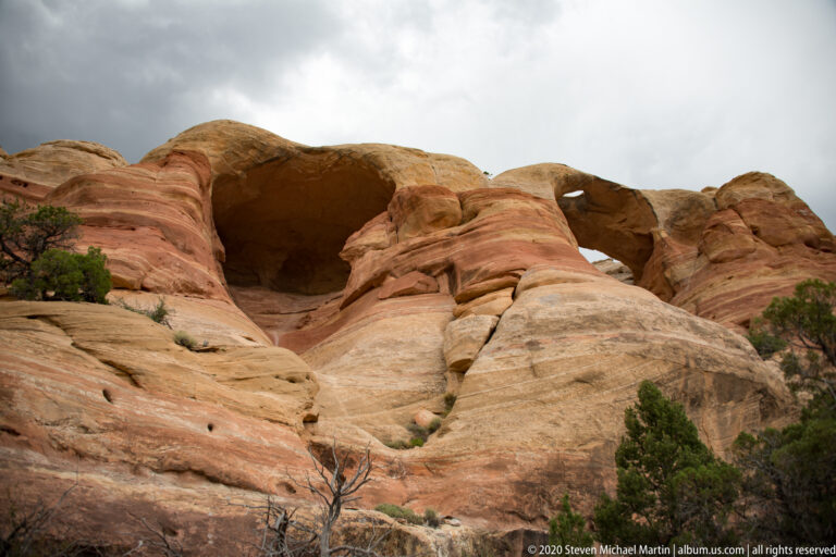Two dark alcoves open in a rounded sandstone wall above a pale sloping rock surface.