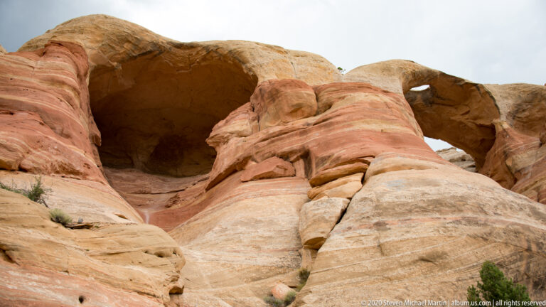 A broad sandstone arch spans a dark alcove above smooth red and cream rock.