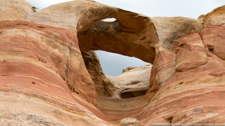 A thick sandstone span crosses overhead between rounded rock walls, framing the sky.