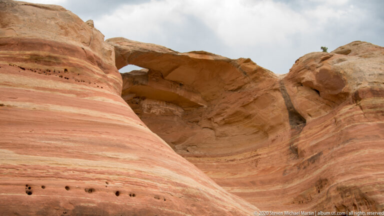 A shallow arch opens over a broad alcove in a smooth red sandstone wall.