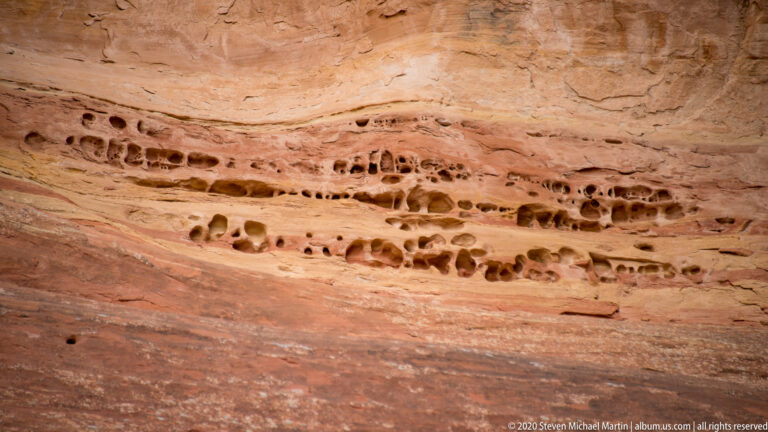 A horizontal band of small erosion pockets crosses a sloping sandstone wall.