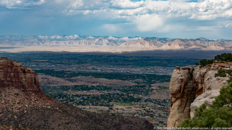 Red canyon walls frame a developed green valley and distant snow-covered mountains.