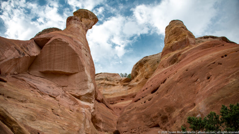 Tall sandstone walls frame a narrow passage open to the cloudy sky.
