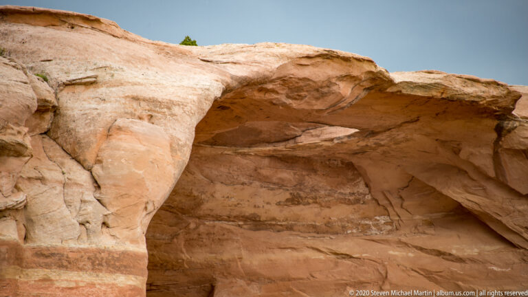 A shallow alcove sits beneath a thick cream sandstone overhang above orange bands.