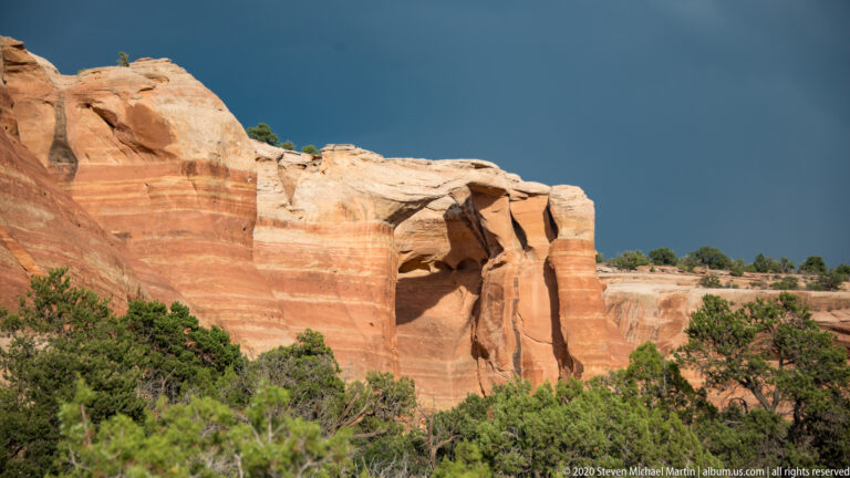 A sandstone arch crosses a cleft between rounded rock masses above scrub.