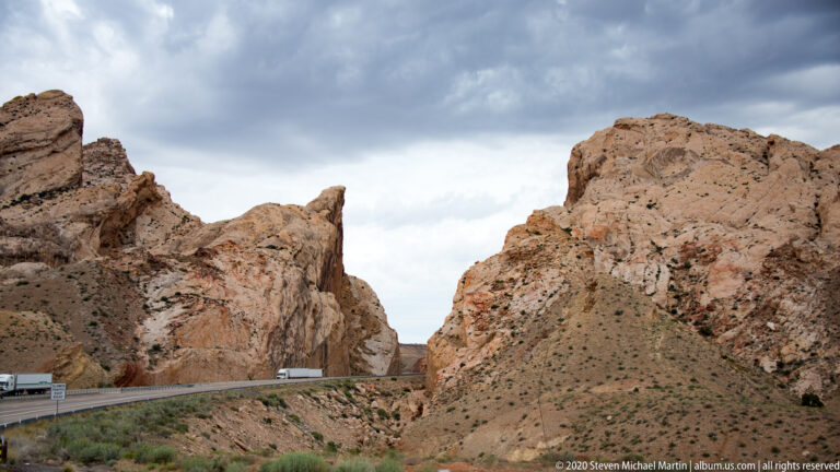 A highway and small truck pass through a narrow gap between pale rock walls.