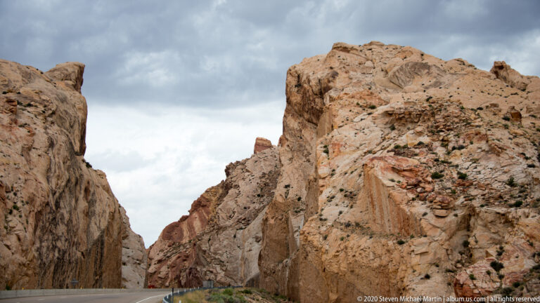 A vehicle follows a road through a narrow pass framed by steep sandstone walls.