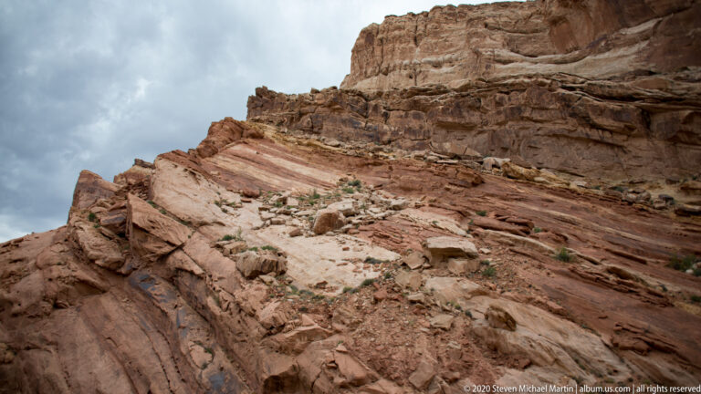 Inclined cream and salmon rock beds fracture into slabs beneath a blocky cliff.