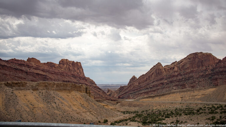A road follows a narrow canyon between dark walls toward a distant basin.