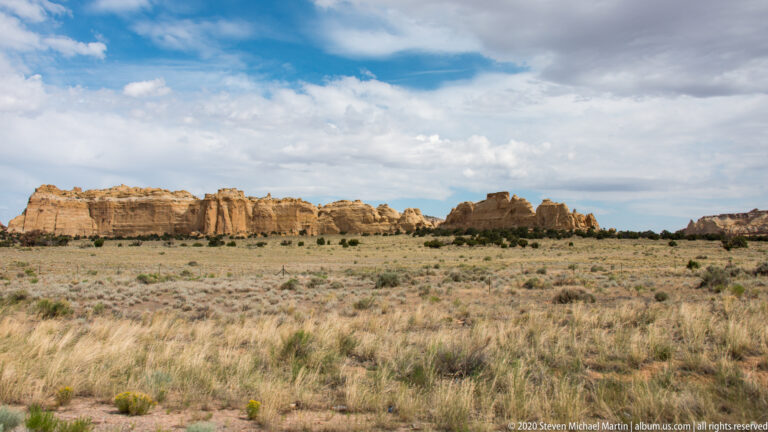 A pale sandstone escarpment runs across a grassy desert plain beneath clouds.