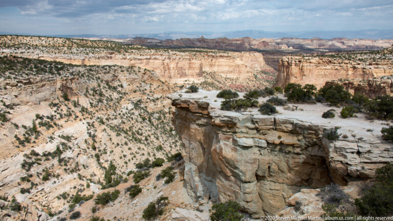 A rocky ledge overlooks a broad canyon with pale shelves and distant cliffs.