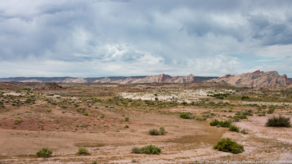A broad scrub basin leads toward a distant line of pale and red rock ridges.