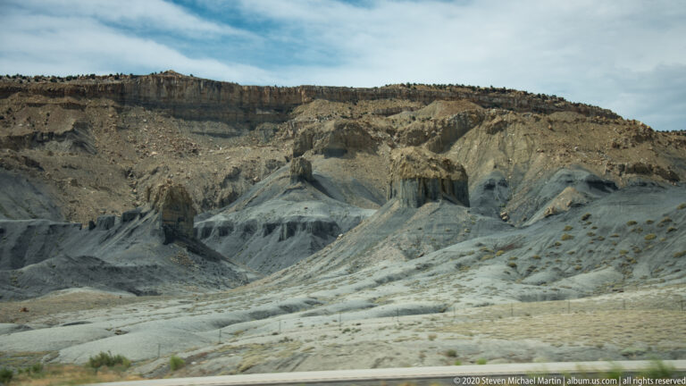 Pale gray gullied slopes and dark rock faces lie below a horizontal ridge, with a road at the bottom.