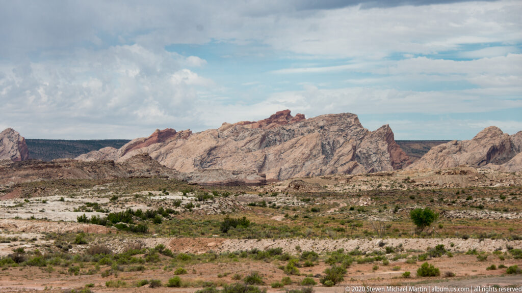 Low desert scrub stretches toward a rugged cream and rust-colored ridge beneath clouds.